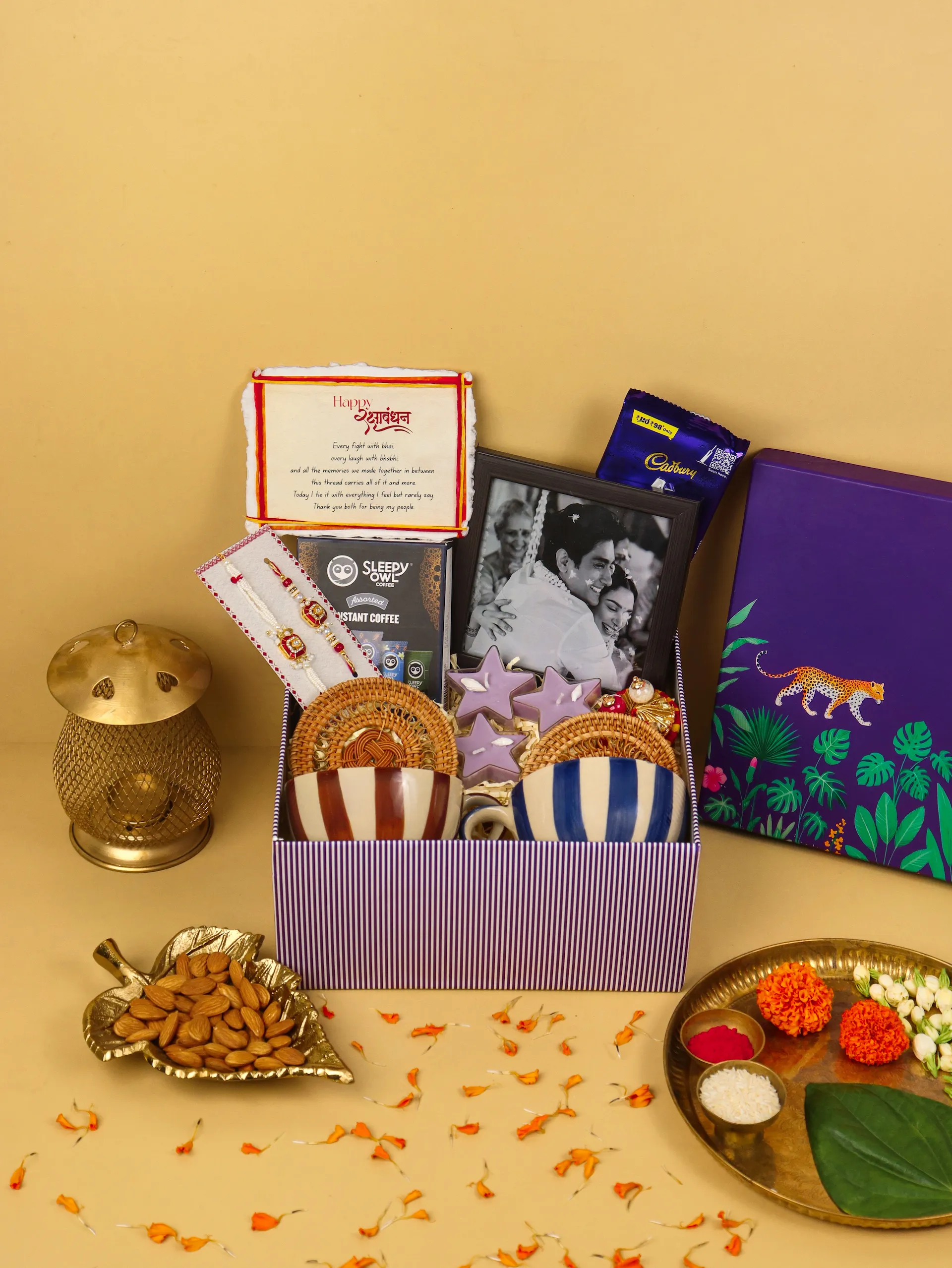 A deep aubergine Wrapscene hamper resting on cream linen, a handcrafted rakhi draped across its lid in soft window light.